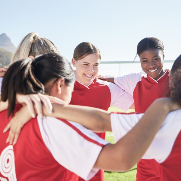 A group of young women athletes huddling and smiling.