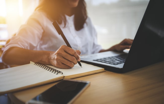 Lady taking notes while working on a laptop