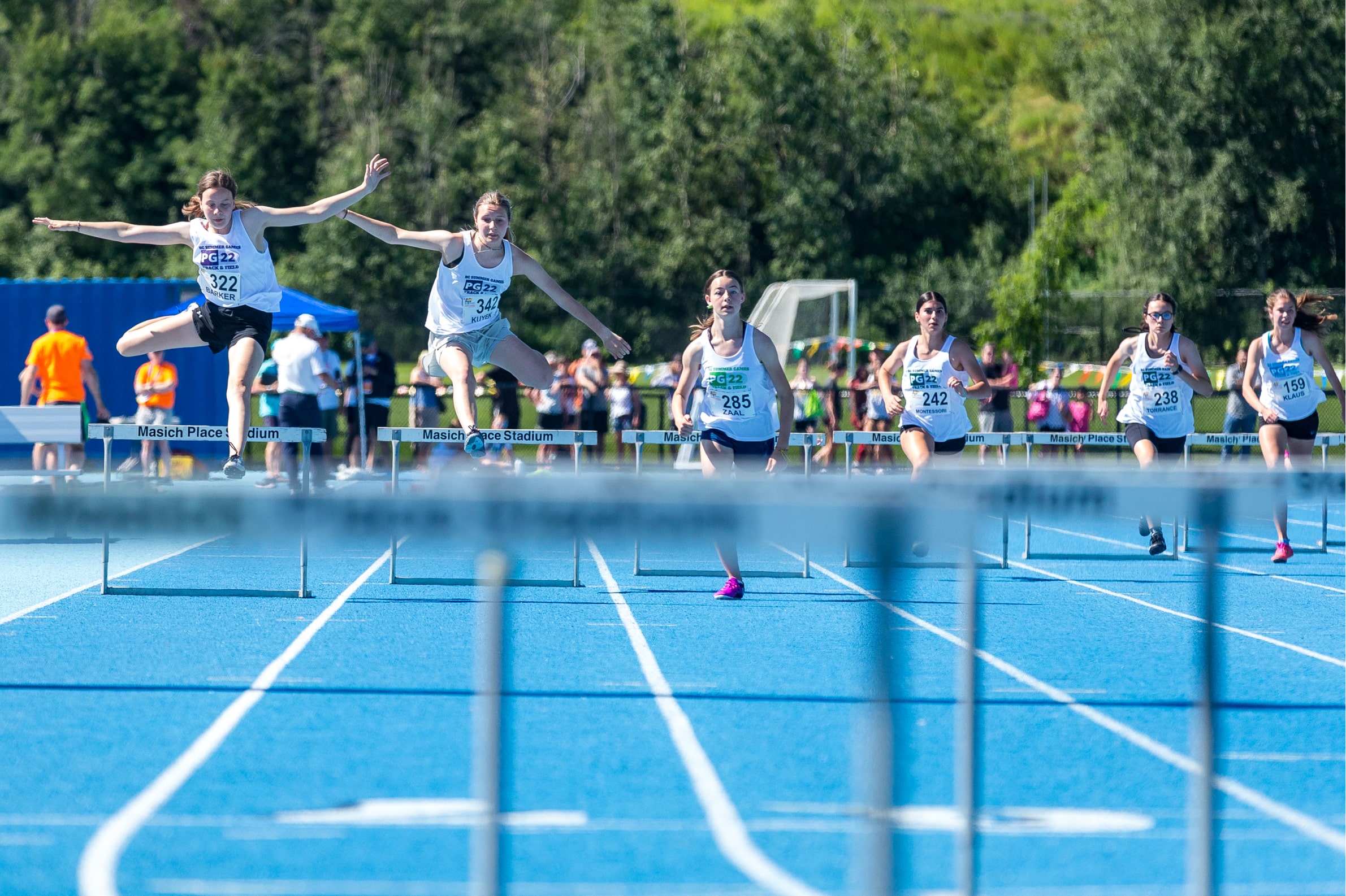 Athlete contestants competing on a running track with hurdles ahead of them